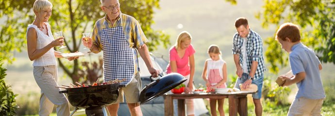 Rodzina z dwójką dzieci i dziadkami spędzają czas przy grillu.
