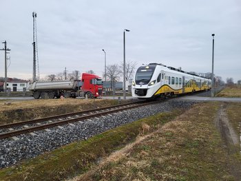 Pociąg pasażerski Kolei Dolnośląskich jedzie po torze, w oddali samochód ciężarowy fot. Radosław Śledziński