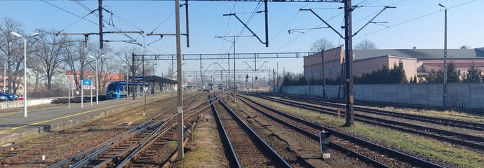 Stacja Racibórz, tory, sieć trakcyjna i pociąg przy peronie w tle, fot. Marek Firla