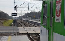 Widok z boku pociągu na tory kolejowe i przejazd kolejowo-drogowy