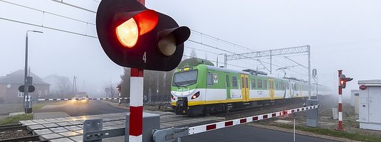 Pociąg na przejeździe, zamknięte rogatki, pulsujące światło