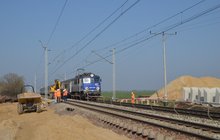 Widać nadjeżdżający do miejsca budowy pociąg IC. Obok elementy do budowy peronu, piach i pracownicy w kaskach. Fot. M. Pabiańska