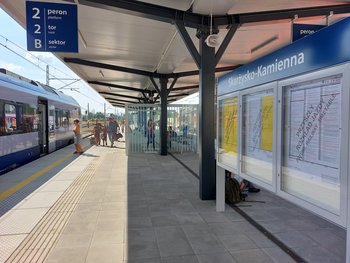 Gablota z informacją o rozkładzie na peronie w Skarżysku-Kamiennej, w tle podróżni i pociąg. fot. Iza Miernikiewicz