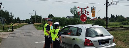 Policjanci podczas akcji ulotkowej stoją obok samochodu przed przejazdem.