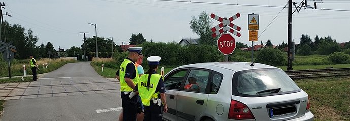 Policjanci podczas akcji ulotkowej stoją obok samochodu przed przejazdem.