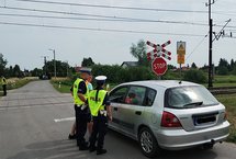 Policjanci podczas akcji ulotkowej stoją obok samochodu przed przejazdem.