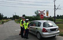 Policjanci podczas akcji ulotkowej stoją obok samochodu przed przejazdem.