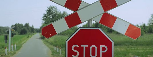 Krzyż św. Andrzeja, znak STOP, w tle przejazd i droga