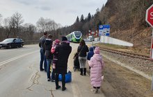 Pociąg zbliżający się do stacji na kolejowym przejściu granicznym w Krościenku. Na pierwszym planie kilkuosobowa grupa uchodźców z Ukrainy – dzieci i dorośli – czekająca na transport do Polski