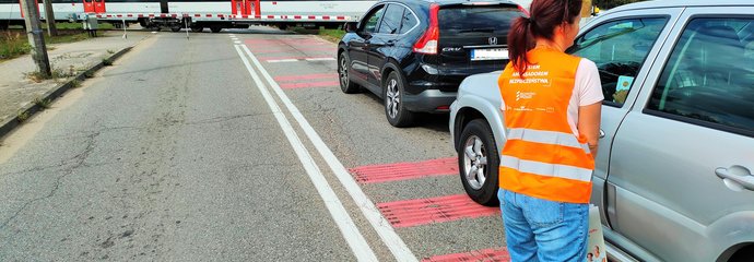 Akcja Bezpieczny Piątek - w miejscowości Mosty. k. Lęborka - samochody przed przejazdem, przedstawiciel PLK rozdaje ulotki. W oddali przejeżdża pociąg fot. Przemysław Zieliński.jpg