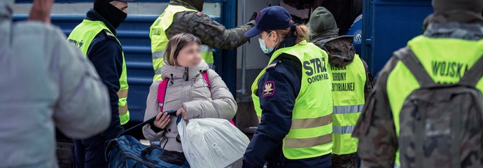 Funkcjonariuszka Straży Ochrony Kolei rozmawia z pasażerką – uchodźczynią z Ukrainy na peronie. W tle pozostali funkcjonariusze pomagają podróżnym wysiąść z ewakuacyjnego pociągu. Fot. Tomasz Jaskot