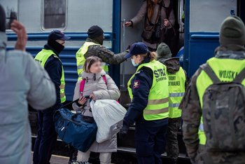 Funkcjonariuszka Straży Ochrony Kolei rozmawia z pasażerką – uchodźczynią z Ukrainy na peronie. W tle pozostali funkcjonariusze pomagają podróżnym wysiąść z ewakuacyjnego pociągu. Fot. Tomasz Jaskot
