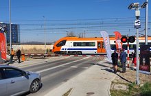 Pracownicy PLK oraz funkcjonariusze Straży Ochrony Kolei stoją przy przejeździe kolejowo-drogowym. Widoczne auto, przejazd kolejowy i pociąg. Fot. Piotr Hamarnik