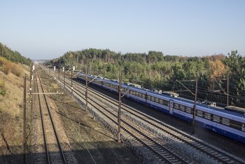 Widok na kilka torów i przejeżdżający pociąg na Centralnej Magistrali Kolejowej. fot. Iza Miernikiewicz