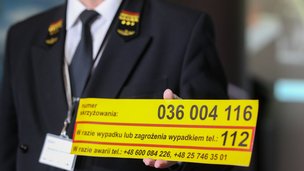 Osoba w mundurze kolejowym trzyma w ręku żółtą naklejkę PLK