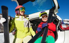 Dwoje dzieci z nartami opartych o bagażnik samochodu