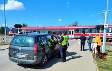 Samochód przed przejazdem, funkcjonariusze SOK rozdają ulotki, w tle pociąg. fot. Przemysław Zieliński PKP PLK