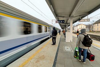Peron w Szamotułach, przejeżdżający pociąg z lewej strony, 3 podróżnych na peronie