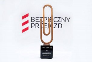 Statuetka w formie spinacza, na tle logotypu kampanii Bezpieczny Przejazd