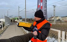 Przedstawiciel PLK pokazuje dziennikarce żółtą naklejkę. W tle pociąg; fot. Anna Znajewska-Pawluk