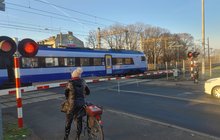 Rowerzystka przed zamkniętymi rogatkami przejazdu na Starołęce, obok sygnalizacja, w tle pociąg_fot.Radek Śledziński