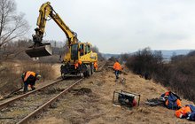 Linia kolejowa nr 108, odcinek Uherce - granica państwa. Robotnicy PLK w odblaskowych, pomarańczowych kombinezonach roboczych pracują na torach. Widoczny specjalistyczny sprzęt. W tle górski, leśny krajobraz. Fot. Piotr Hamarnik, zdjęcie nr 1