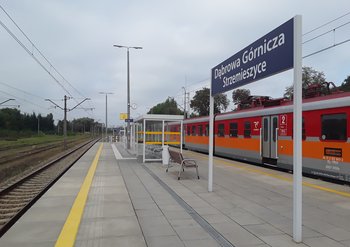 Stacja Dąbrowa Górnicza Strzemieszyce, na peronie wiata i ławka, tablica z nazwą stacji i pociąg regionalny, fot. Mateusz Kozłowski