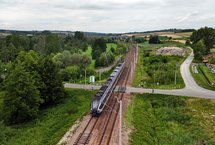 Pociąg przejeżdża przez przejazd kolejowo-drogowy w Szczepanowicach, w miejscu gdzie powstaną nowe perony, widok z lotu ptaka, fot. Piotr Hamarnik