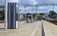 Pasażerowie na przystanku kolejowym, an pierwszym planie widać wyświetlacz z rozkładem jazdy, fot. Mateusz Ostrzyżek