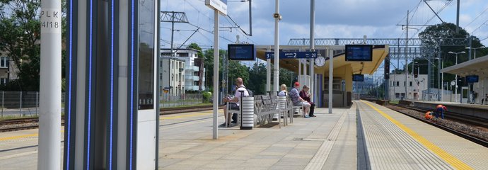 Pasażerowie na przystanku kolejowym, an pierwszym planie widać wyświetlacz z rozkładem jazdy, fot. Mateusz Ostrzyżek