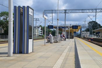 Pasażerowie na przystanku kolejowym, an pierwszym planie widać wyświetlacz z rozkładem jazdy, fot. Mateusz Ostrzyżek