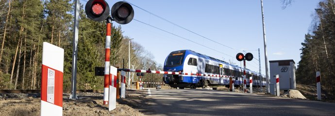 Przejazd kolejowo-drogowy z zamkniętymi rogatkami i przejeżdżającym pociągiem