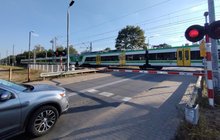 Przejazd kolejowo-drogowy w Sulejówku, samochód czeka przed rogatkami, w tle jadący pociąg; fot. Rafał Wilgusiak