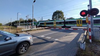 Przejazd kolejowo-drogowy w Sulejówku, samochód czeka przed rogatkami, w tle jadący pociąg; fot. Rafał Wilgusiak
