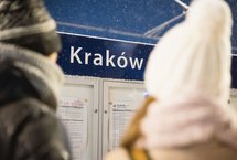 Podróżni stojący przed tablicą z rozkładem jazdy.