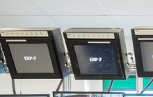 Pracownik siedzący tyłem przy biurku, patrzący w stronę kilkunastu monitorów.