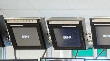 Pracownik siedzący tyłem przy biurku, patrzący w stronę kilkunastu monitorów.