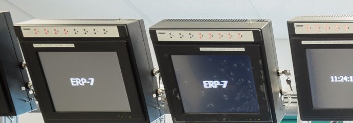 Pracownik siedzący tyłem przy biurku, patrzący w stronę kilkunastu monitorów.