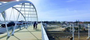 Piesi i rowerzyści idą po nowym wiadukcie w Łowiczu. Na jezdni sznur aut. W tle tory kolejowe i sieć trakcyjna. Fot. Anna Jadaś