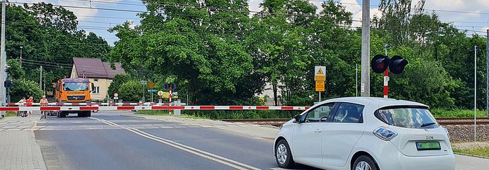 Przejazd kolejowo-drogowy zamkniętymi rogatkami. Samochody przed szlabanem.