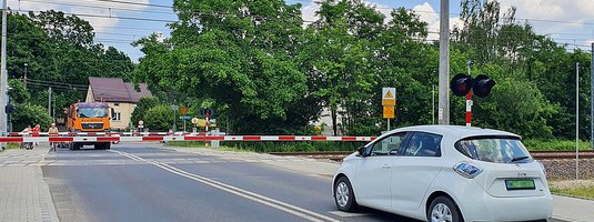 Przejazd kolejowo-drogowy zamkniętymi rogatkami. Samochody przed szlabanem.