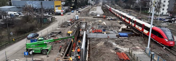 Maszyny i wykonawcy na budowie przejścia podziemnego stacji Warszawa Wawer, obok po torze jedzie pociąg, fot. Łukasz Bryłowski