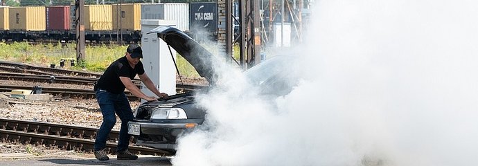 Kierowca, przy unieruchomionym na przejeździe, dymiącym samochodzie.