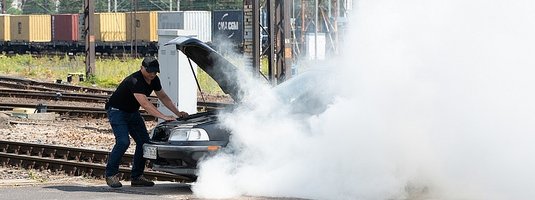 Kierowca, przy unieruchomionym na przejeździe, dymiącym samochodzie.