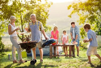 Rodzina z dwójką dzieci i dziadkami spędzają czas przy grillu.