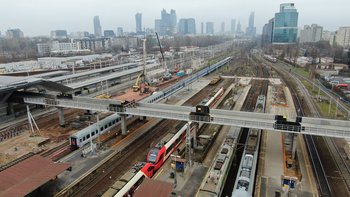 Widok z góry na kładkę nad peronami stacji. Pociągi na torach. W tle widok na centrum Warszawy. Fot. Artur Lewandowski