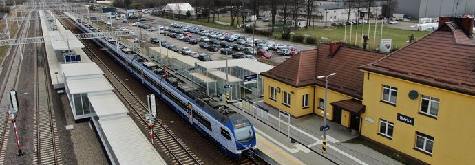 Widok z góry na stację w Warce, widać pociag przy peronie, budynek dworca i parkujące samochody, fot. A.Lewandowski, P.Mieszkowski