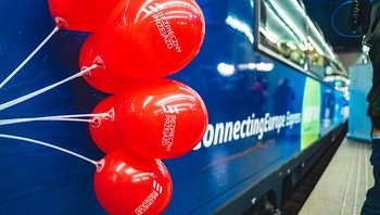 Kilka balonów kampanii na tle pociągu Connecting Europe Express, który stoi przy peronie.