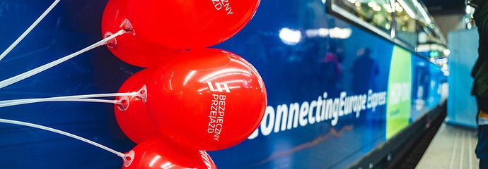 Kilka balonów kampanii na tle pociągu Connecting Europe Express, który stoi przy peronie. 