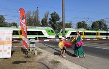 Dzieci z dmuchanymi zabawkami czekają z mamą przed zamkniętymi rogatkami, przejeżdża pociąg fot. Anna Znajewska-Pawluk